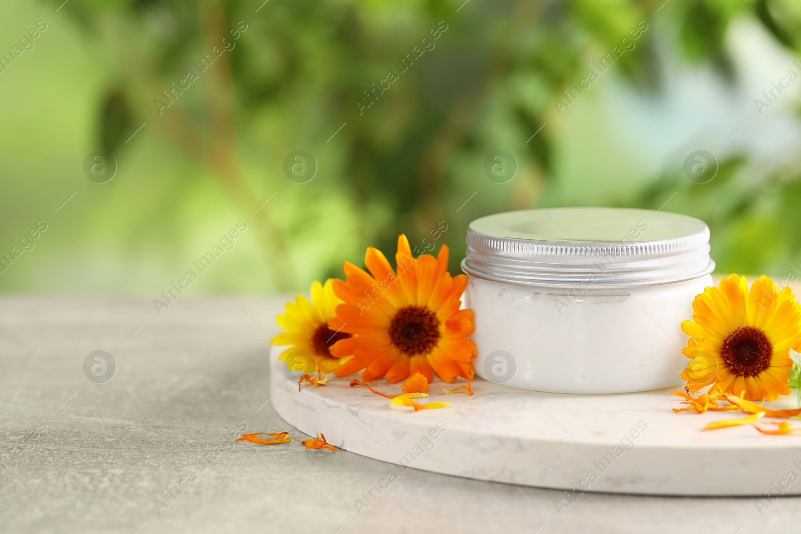 Photo of Jar of cream and beautiful calendula flowers on light grey table outdoors, closeup. Space for text