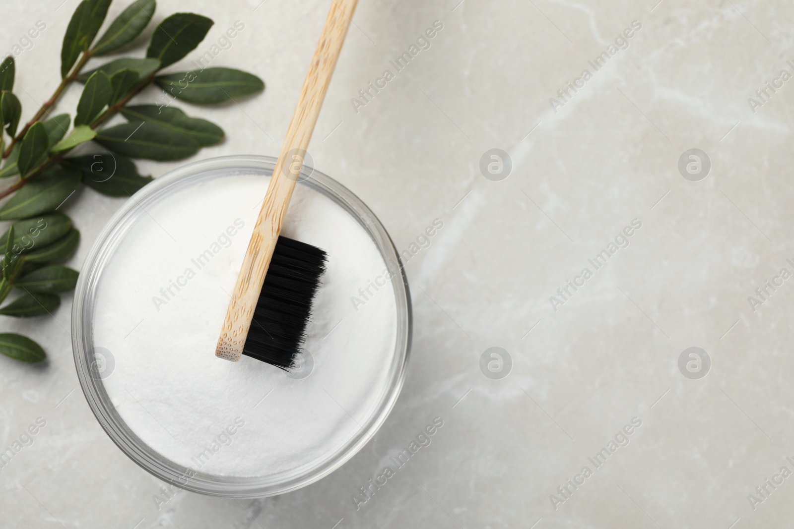 Photo of Bamboo toothbrush, glass bowl of baking soda and green leaves on light marble table, flat lay. Space for text