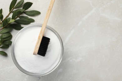 Photo of Bamboo toothbrush, glass bowl of baking soda and green leaves on light marble table, flat lay. Space for text