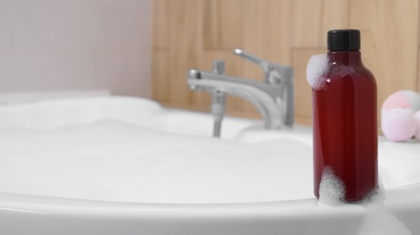 Photo of Red bottle of bubble bath on tub indoors, space for text