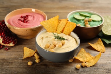 Photo of Different kinds of tasty hummus, nachos and ingredients on wooden table