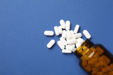 Photo of Vitamin pills and bottle on blue background, top view. Space for text