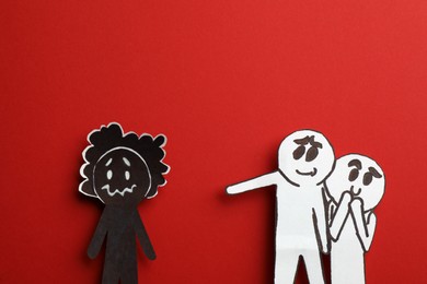Photo of White paper figures mocking at black one on red background, flat lay. Racism concept