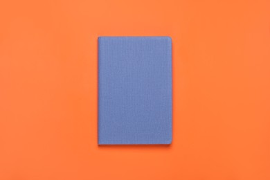 Photo of Closed blue notebook on orange background, top view