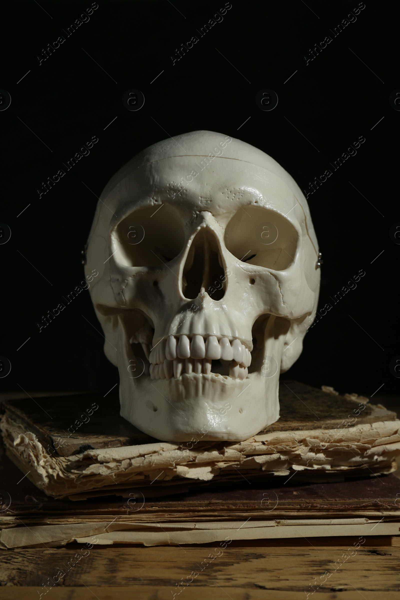 Photo of Human skull and old book on wooden table against black background