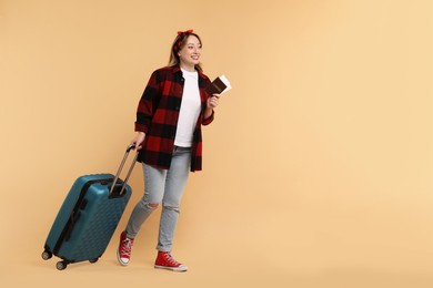 Photo of Happy young woman with passport, ticket and suitcase on beige background, space for text