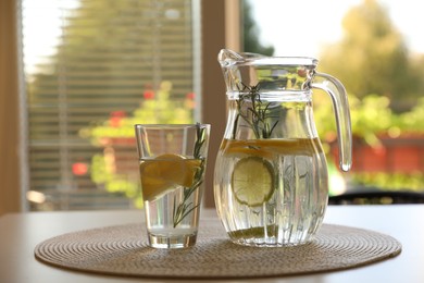 Photo of Jug and glass with refreshing lemon water on light table indoors