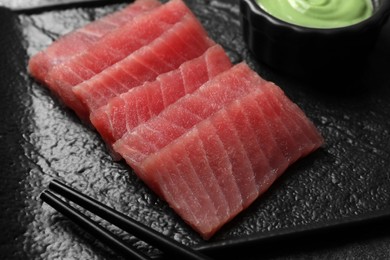 Photo of Tasty sashimi (pieces of fresh raw tuna) on black plate, closeup