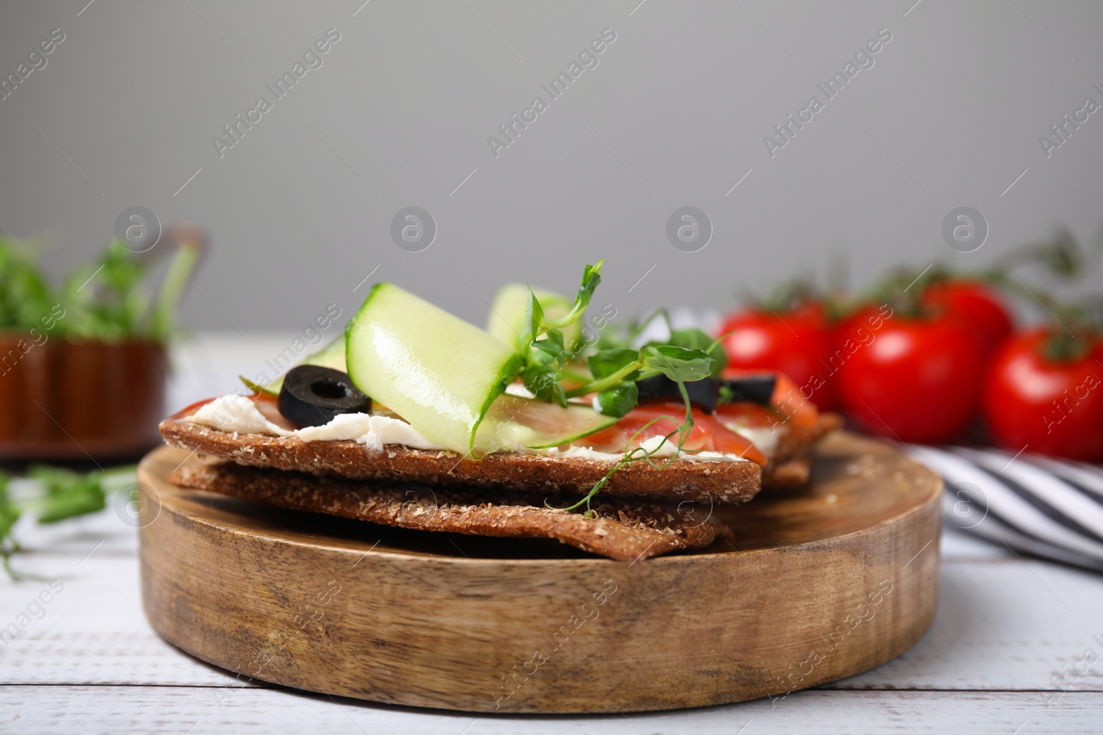 Photo of Tasty rye crispbreads with salmon, cream cheese and vegetables on white wooden table, closeup