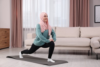 Muslim woman in hijab doing exercise on fitness mat at home. Space for text