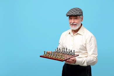 Man with chessboard and game pieces on light blue background. Space for text