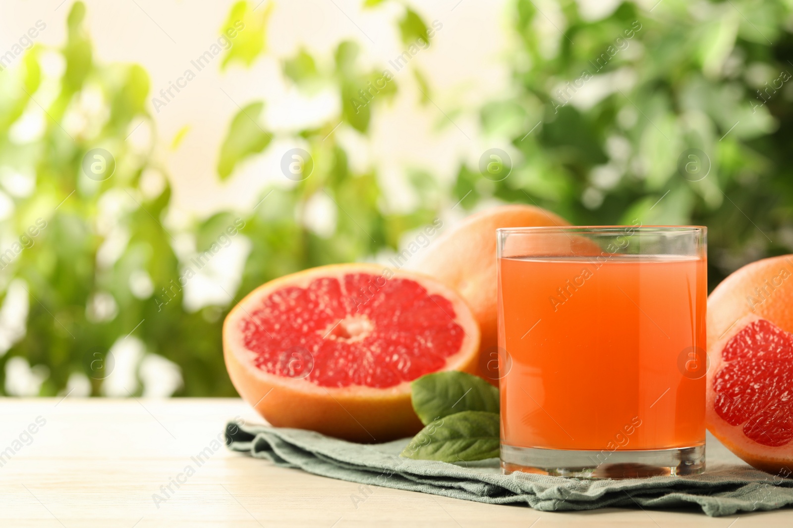 Photo of Glass of delicious grapefruit juice on white table against blurred background, space for text