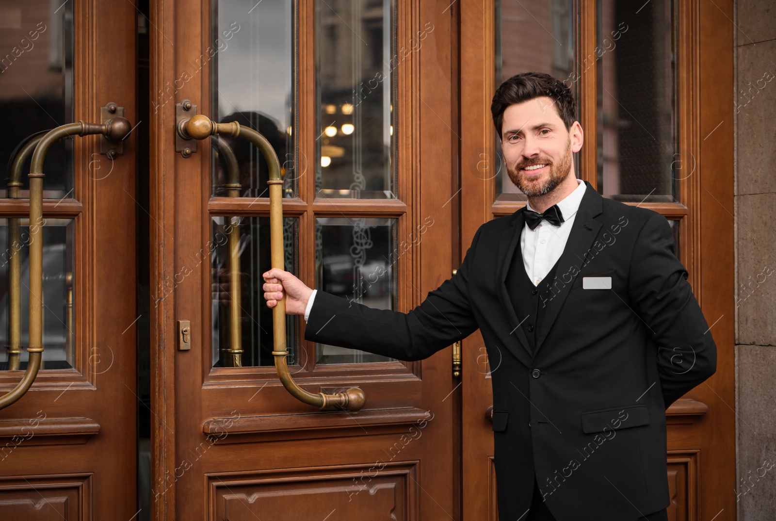 Photo of Butler in elegant suit opening wooden hotel door. Space for text