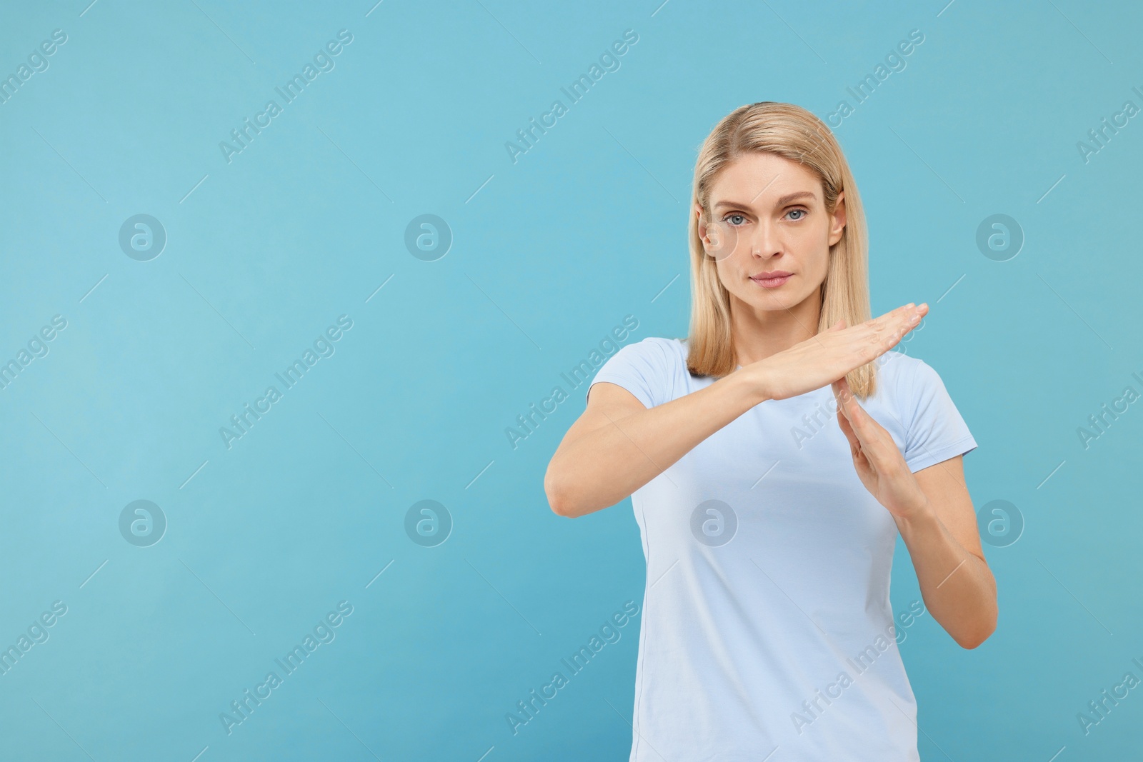 Photo of Woman showing time out gesture on light blue background, space for text. Stop signal