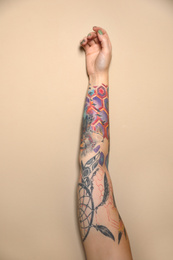 Photo of Woman with colorful tattoos on arm against beige background, closeup