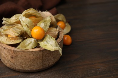 Photo of Ripe physalis fruits with calyxes in bowl on wooden table, closeup. Space for text