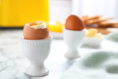 Cups with soft boiled eggs on marble table, space for text. Healthy breakfast