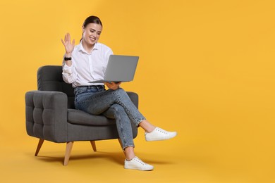 Photo of Happy woman with laptop sitting in armchair on orange background. Space for text