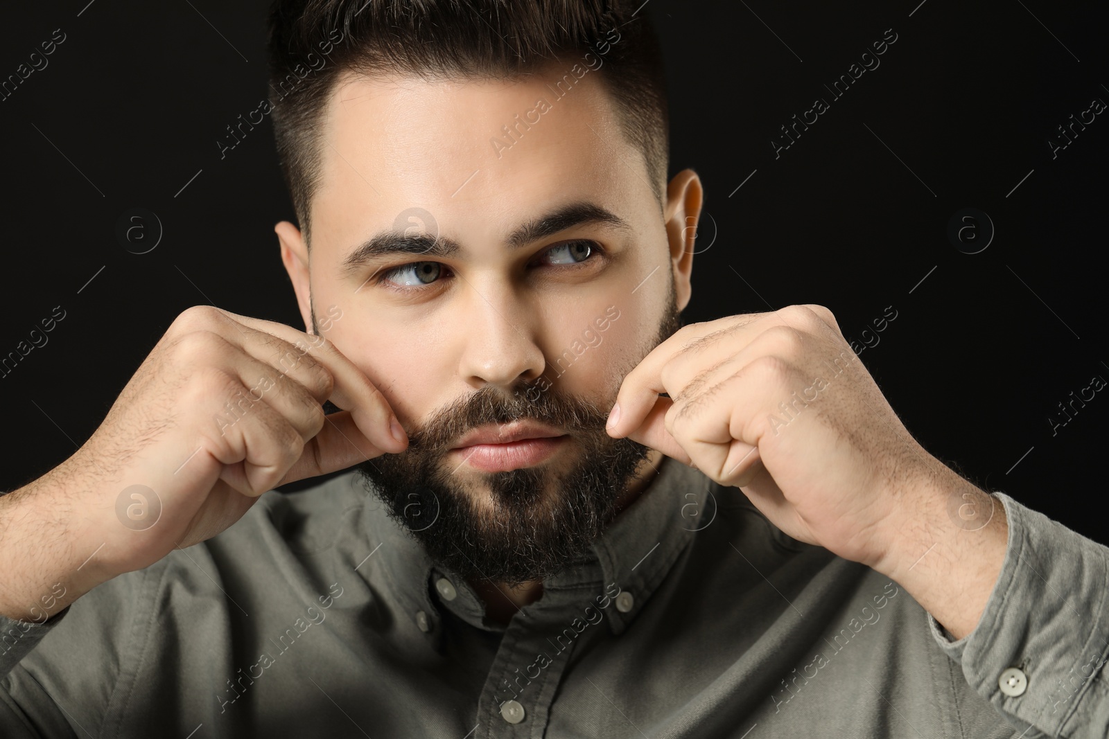 Photo of Young man in shirt touching mustache on black background