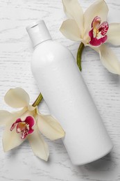 Photo of Bottle of shampoo and flowers on white wooden table, flat lay