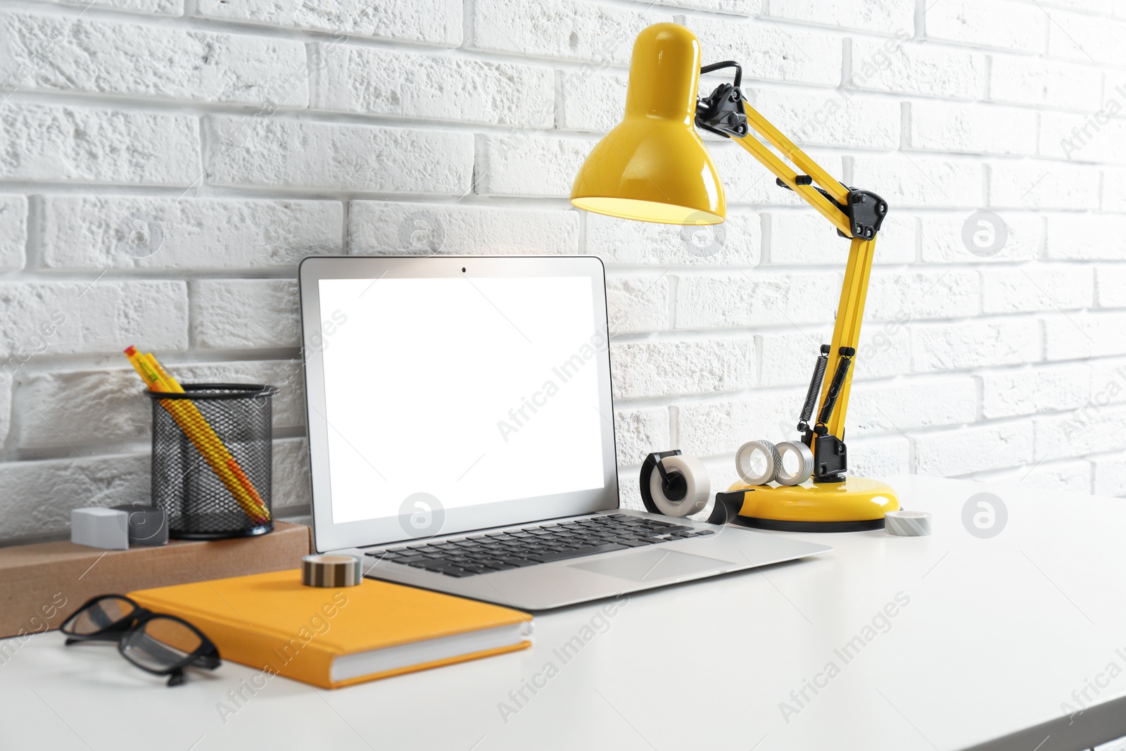 Photo of Modern workplace with laptop and lamp on table near brick wall. Space for design