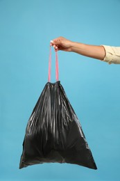 Photo of Woman holding full garbage bag on light blue background, closeup