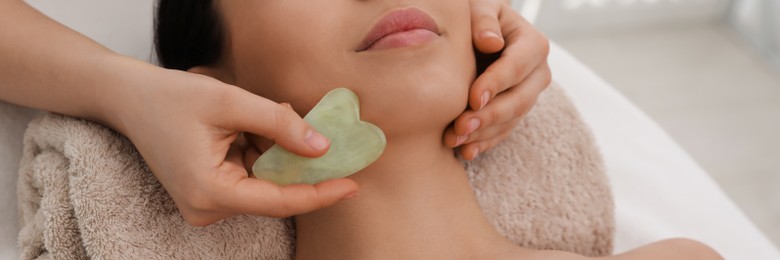 Young woman receiving facial massage with gua sha tool in beauty salon. Banner design