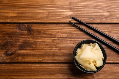 Pickled ginger in bowl and chopsticks on wooden table, flat lay. Space for text