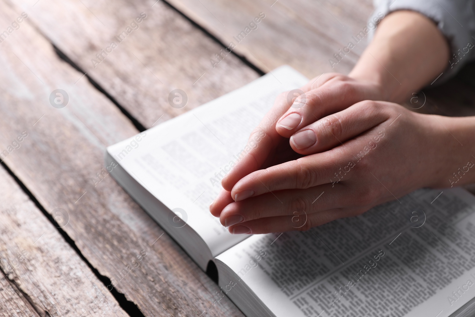 Photo of Religion. Christian woman praying over Bible at wooden table, closeup