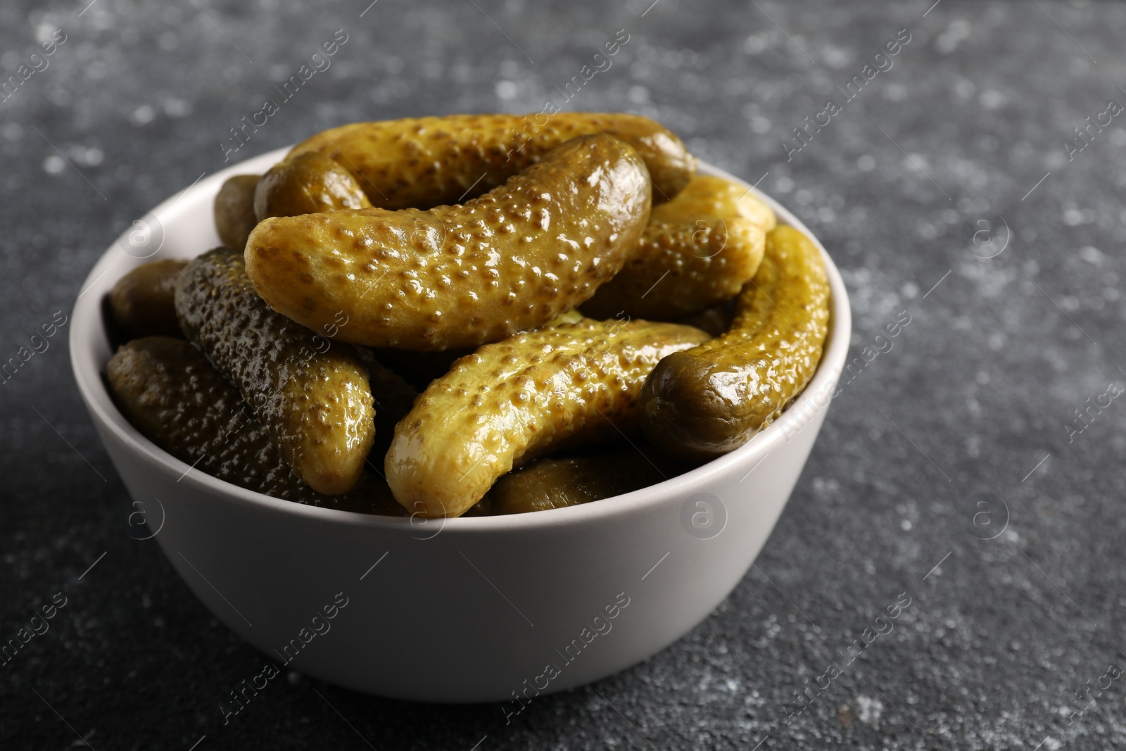 Photo of Tasty pickled cucumbers in bowl on grey table, closeup