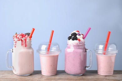 Different tasty milk shakes in mason jars and plastic cups on wooden table