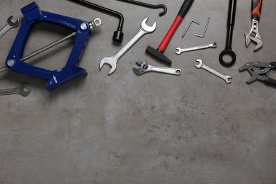 Car scissor jack and different tools on grey surface, flat lay. Space for text