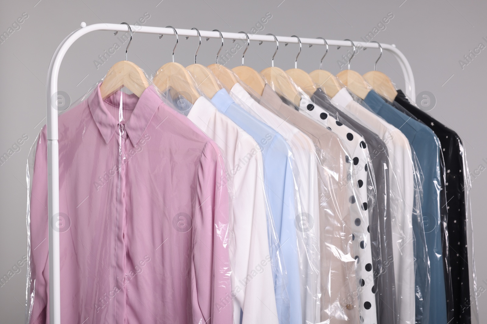 Photo of Dry-cleaning service. Many different clothes in plastic bags hanging on rack against grey background