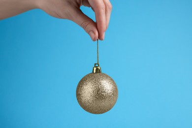 Woman holding glitter Christmas ball on light blue background, closeup