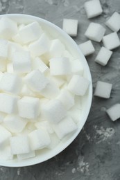 Photo of White sugar cubes in bowl on grey table, top view