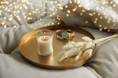 Burning candle, wristwatch and decorative dry plants on golden tray