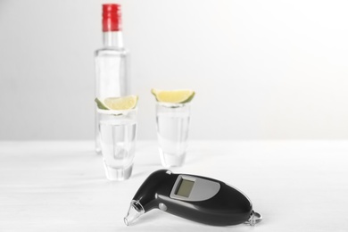 Modern breathalyzer and alcohol on white table. Space for text