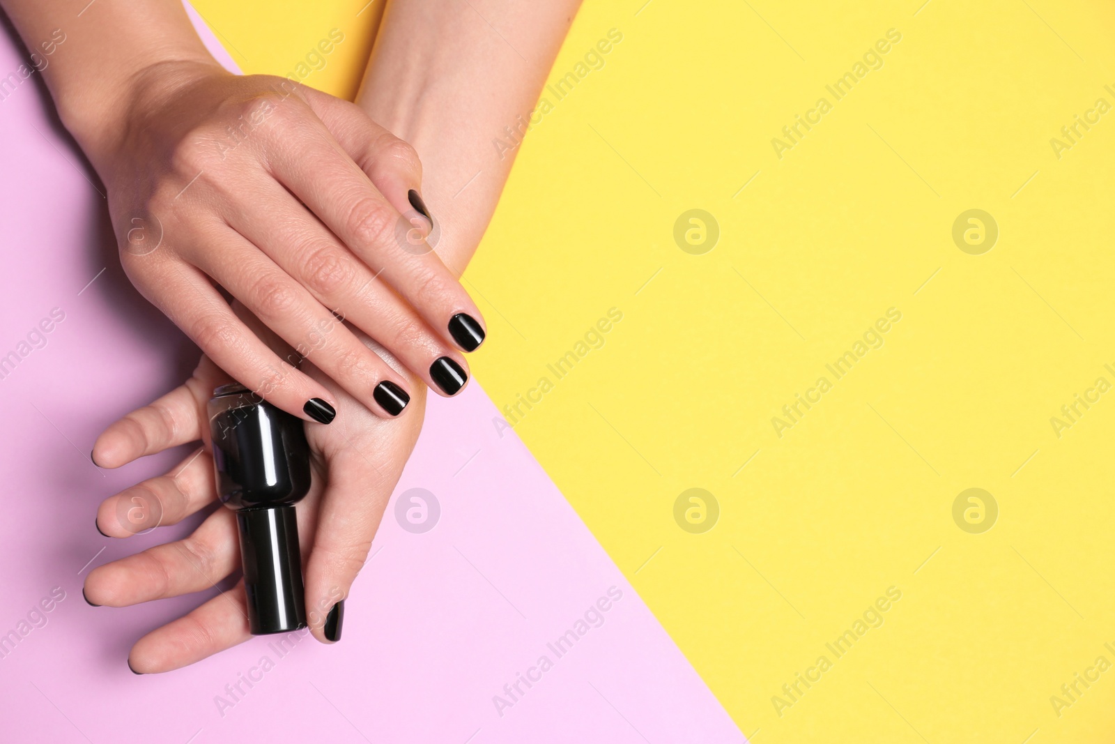 Photo of Woman with black manicure holding nail polish bottle on color background, top view. Space for text