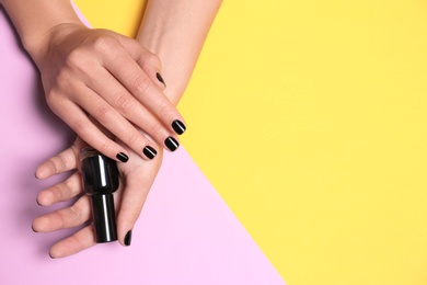 Photo of Woman with black manicure holding nail polish bottle on color background, top view. Space for text