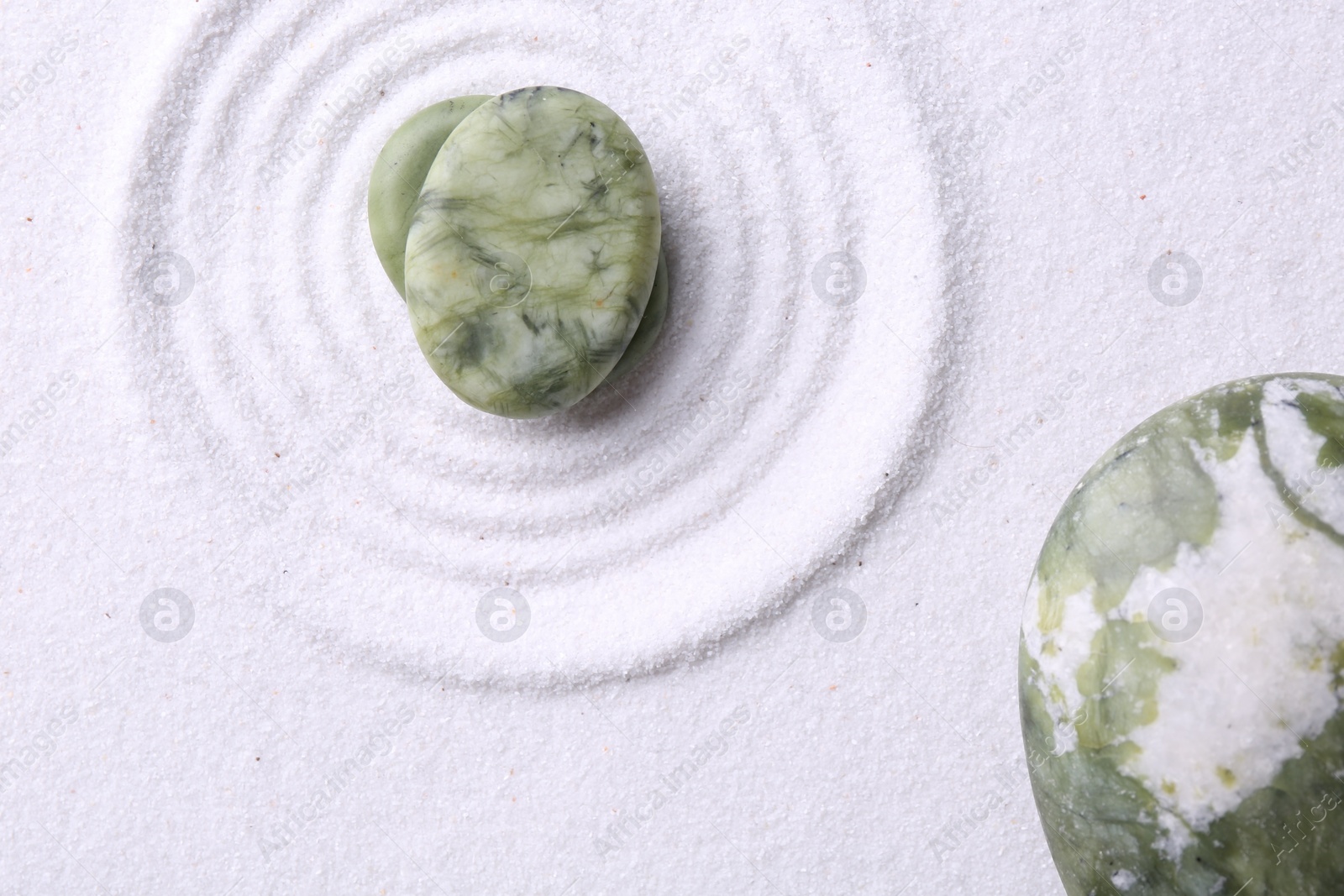 Photo of Zen garden stones on white sand with pattern, flat lay