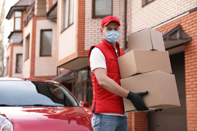 Photo of Courier in protective mask and gloves with boxes near car outdoors. Delivery service during coronavirus quarantine