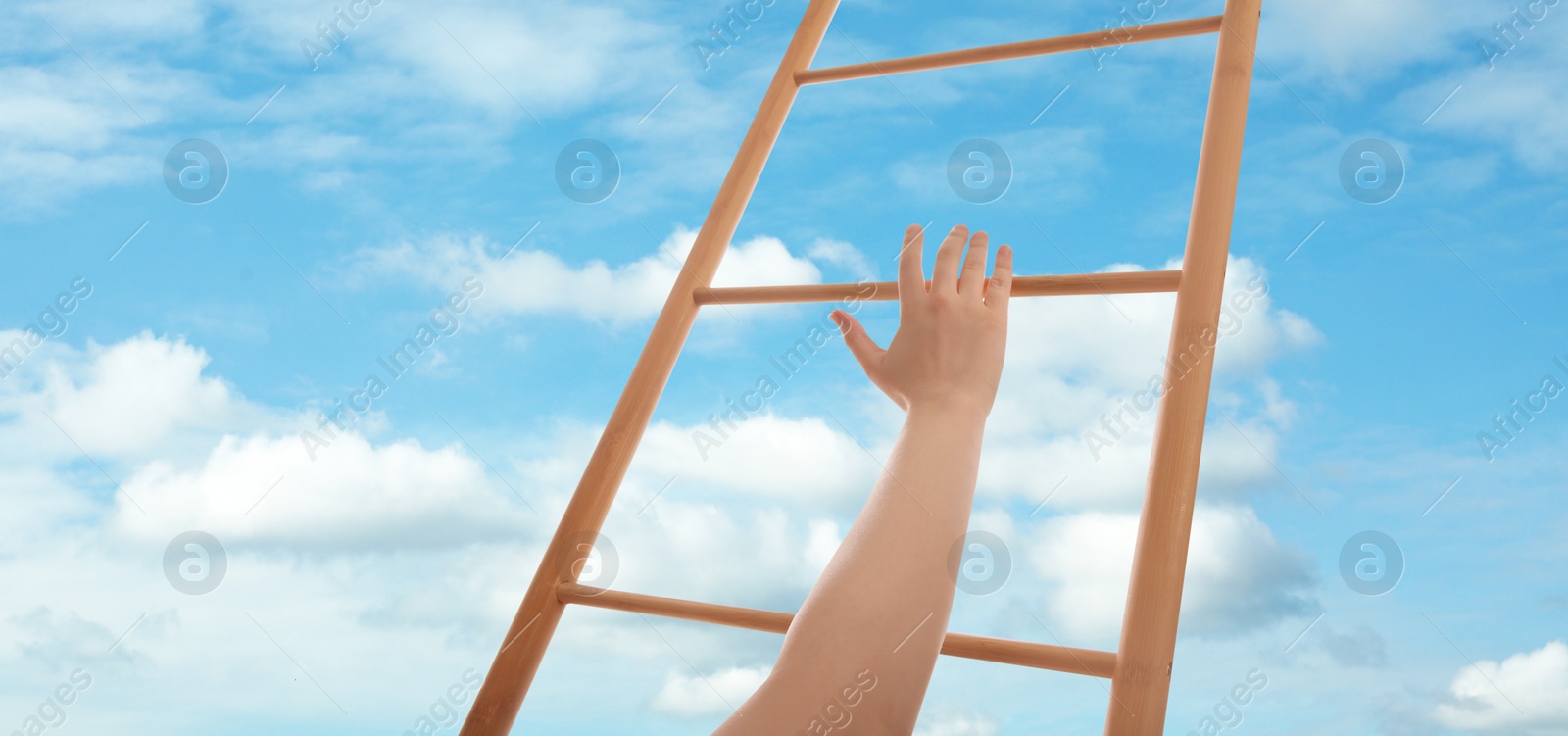 Image of Woman climbing up wooden ladder against blue sky with clouds, closeup. Banner design 