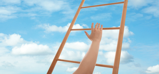 Woman climbing up wooden ladder against blue sky with clouds, closeup. Banner design 