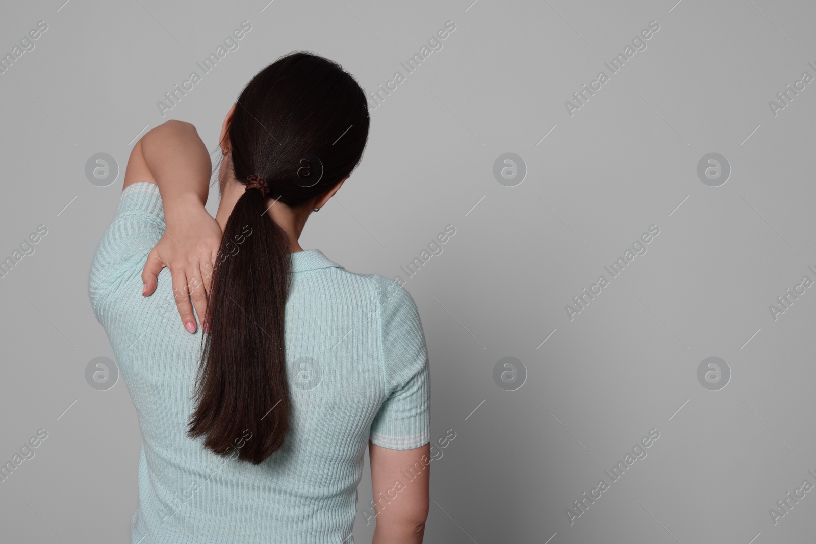 Photo of Young woman suffering from pain in back on light grey background, space for text. Arthritis symptoms