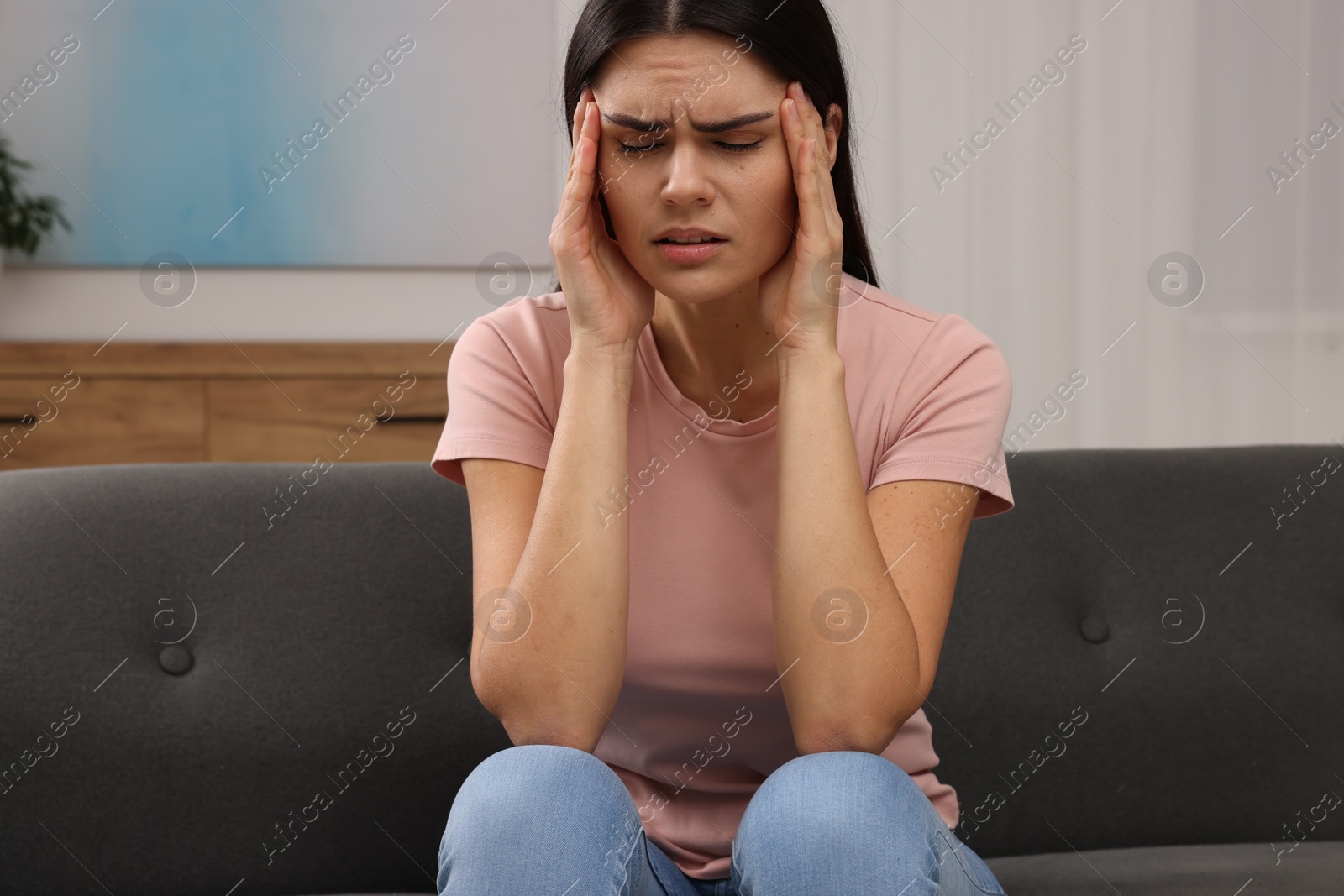 Photo of Sad woman suffering from headache on sofa indoors