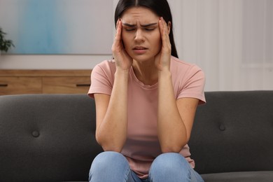 Sad woman suffering from headache on sofa indoors