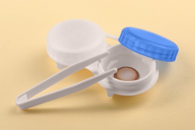 Photo of Case with color contact lenses and tweezers on pale yellow background