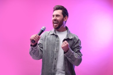 Handsome man with microphone singing on pink background