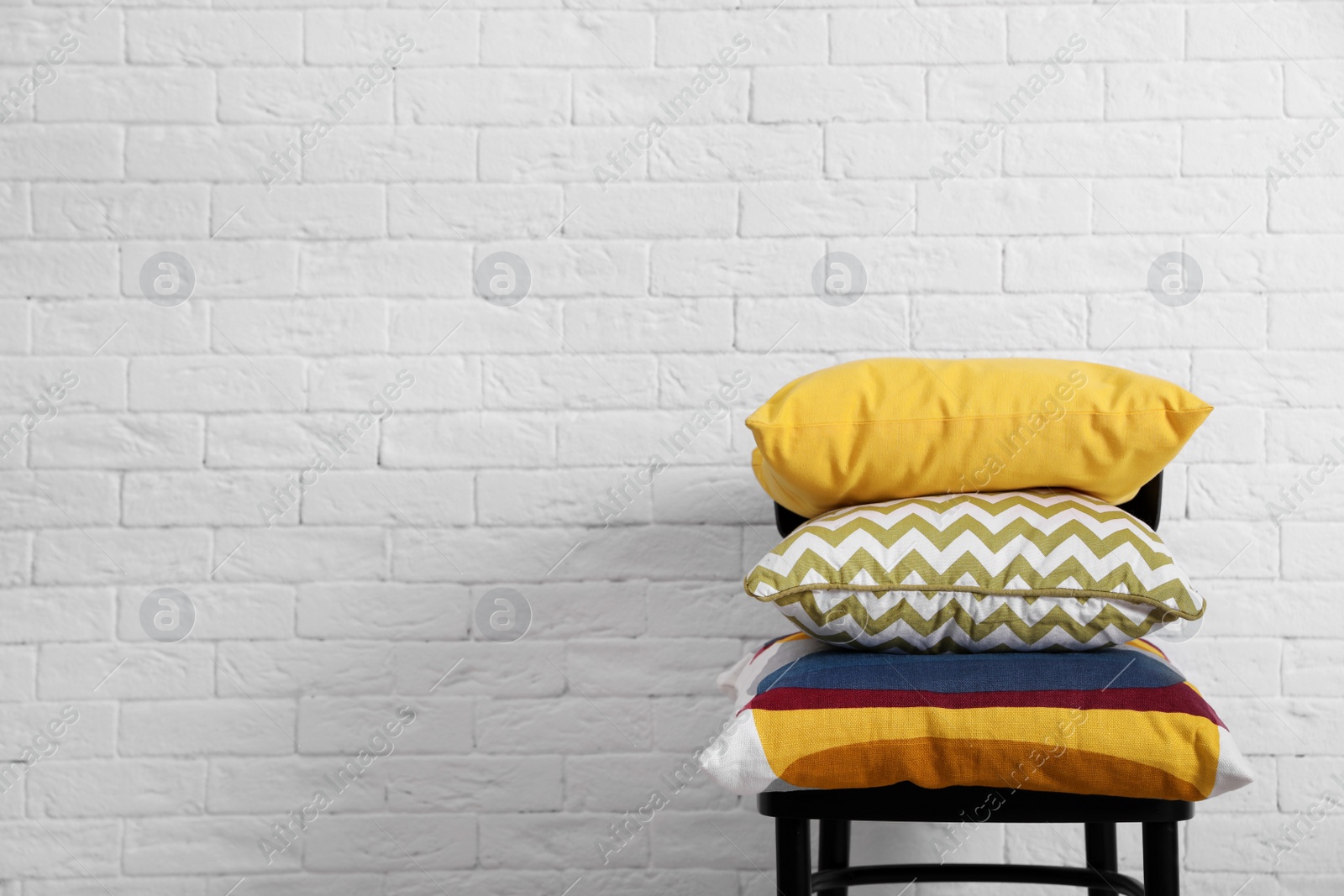 Photo of Many different pillows on chair near brick wall with space for text