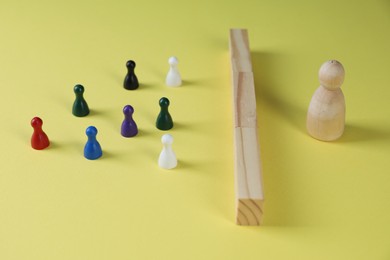 Photo of Barriers and difficulties in communication. Wooden blocks separating small human figures from one big on yellow background, closeup